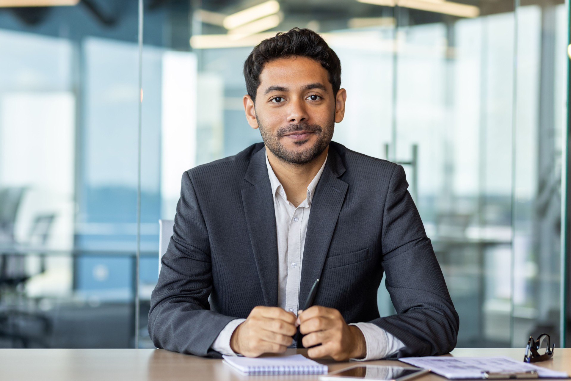 Porträt eines jungen Investor-Bankers am Arbeitsplatz in der Bankfiliale, eines Geschäftsmannes im Business-Anzug, der freundlich in die Kamera blickt, eines Mannes bei der Arbeit